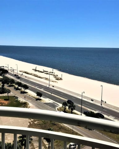 Elevated view of wide sandy beach with coastal road, palm trees, and calm blue ocean under clear sky