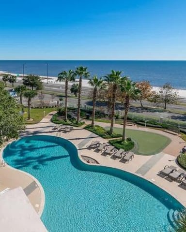 Curved resort pool with ocean view, palm trees, beach access, and lounge chairs