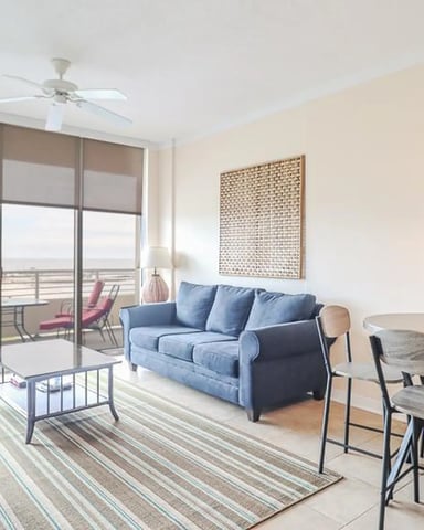 Modern high-rise apartment with blue sofa, dining table, and floor-to-ceiling windows overlooking city and water