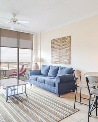 Modern apartment living room with blue sofa, high-rise balcony view, striped area rug, and dining table with bar seating
