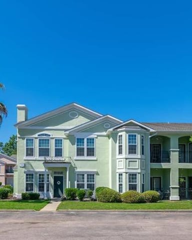 Two-story pale green house with white trim, palm tree, and manicured lawn on residential street