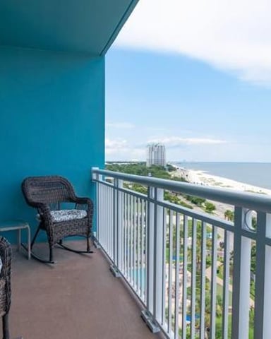 Oceanfront balcony with turquoise walls, wicker chairs, and view of beach and distant high-rise building
