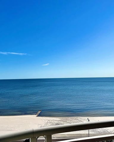 Sandy beach with calm blue ocean and clear sky, viewed from a railing