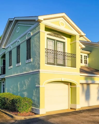 Colorful colonial-style houses with yellow and turquoise facades, balconies, and garage doors on a clear day