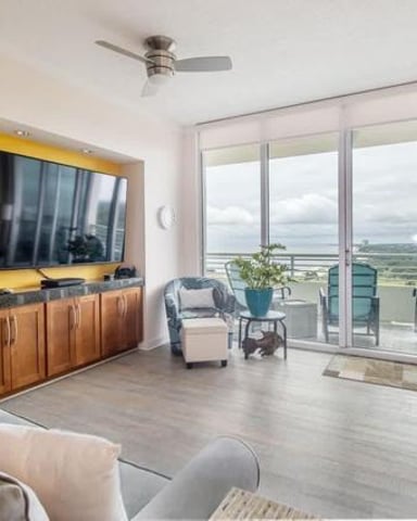 Modern high-rise living room with wall-mounted TV, wood cabinetry, and floor-to-ceiling windows overlooking expansive landscape views