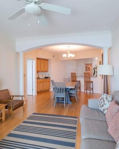 Open-plan living room with gray sofa, wooden TV stand, and archway leading to dining area and kitchen