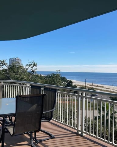 Oceanfront deck with dining table, chairs, and white railing overlooking beach and blue ocean