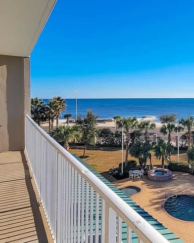 Beachfront balcony with ocean view, pool, palm trees, and sandy beach below