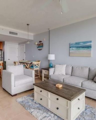 Open-plan living room with gray sofa, white armchair, and kitchen with bar seating in background
