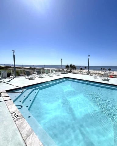 Rooftop swimming pool with ocean view, lounge chairs, and clear blue sky