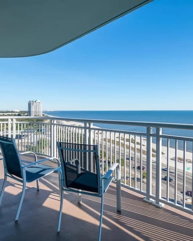 Beachfront balcony with two lounge chairs, white railing, and panoramic ocean and sandy beach view