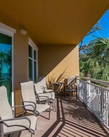 Oceanfront balcony with lounge chairs, white railing, palm trees, and clear blue sky view