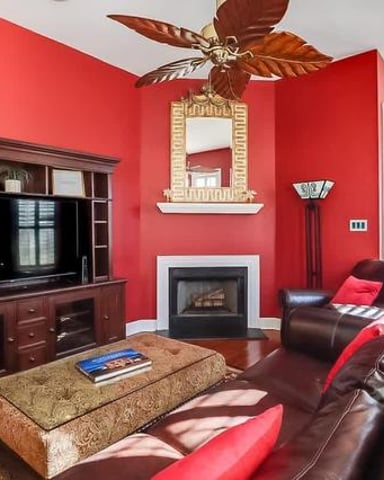 Bright red living room with dark wood entertainment center, fireplace, leather seating, and decorative ceiling fan