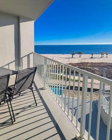 Beachfront balcony with dining table overlooking sandy beach and blue ocean with people in distance