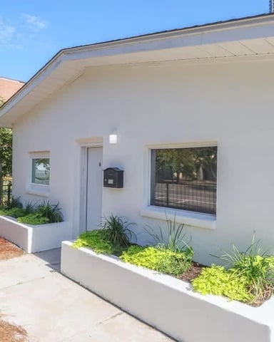 White single-story house numbered 958 with front garden planters, mailbox, and driveway on sunny day