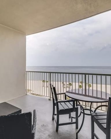 Beachfront balcony with black chairs and ocean view, white railing, sandy beach below