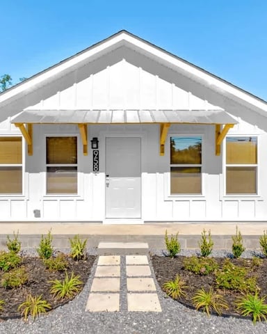 White cottage with yellow trim, metal roof, front porch, and landscaped yard with stepping stones