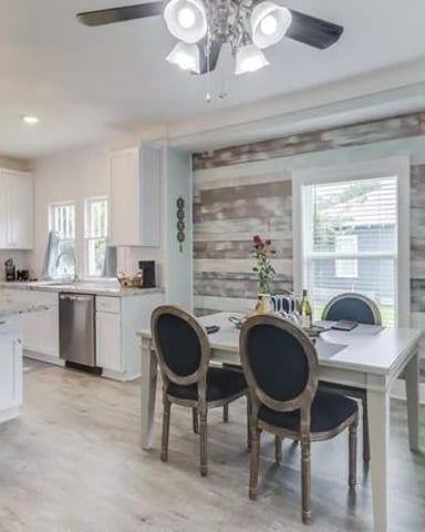 Modern kitchen and dining area with white cabinetry, stainless steel appliances, wood dining table, and sliding glass doors with striped shades.