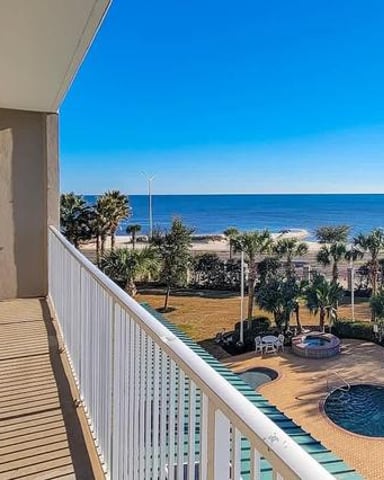 Beachfront balcony with lounge chairs overlooking pool, palm trees, and ocean under clear blue sky