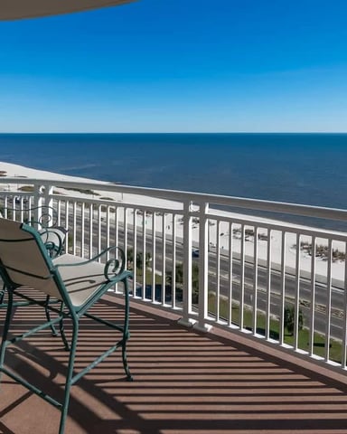 Oceanfront balcony with lounge chair overlooking sandy beach and blue water under clear sky