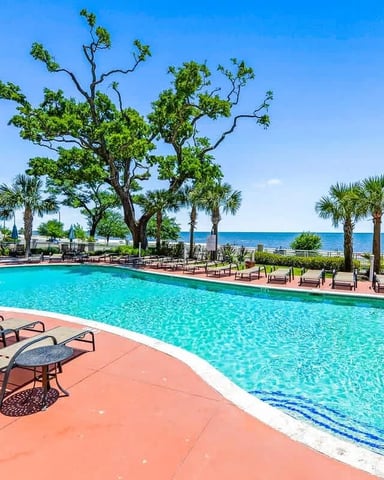 Resort pool with turquoise water, lounge chairs, palm trees, and ocean view beyond white railing