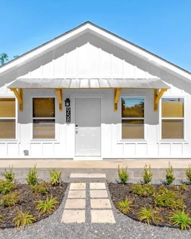 White cottage with yellow-trimmed windows and front door, landscaped front yard with stepping stones