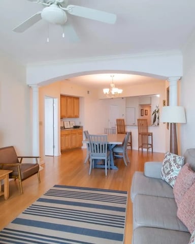 Open-plan living room with gray sofa, TV, wooden dining table, and kitchen visible through archway