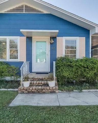Bright blue cottage-style house with white trim, front porch, and attached carport with lattice screening