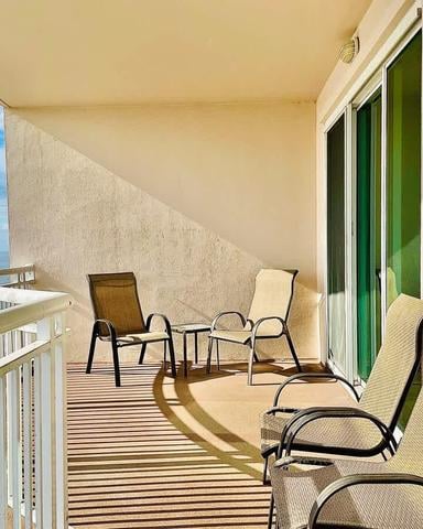 Beachfront balcony with lounge chairs, small table, white railing, and ocean view under retractable awning