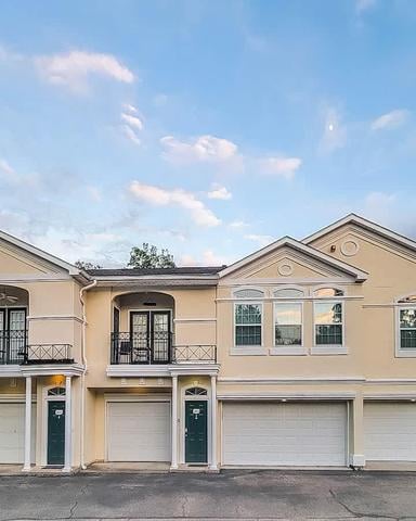 Beige townhouse with three garage doors, peaked roofs, and balconies under blue sky