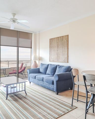 High-rise apartment living room with blue sofa, dining table, and balcony overlooking city skyline