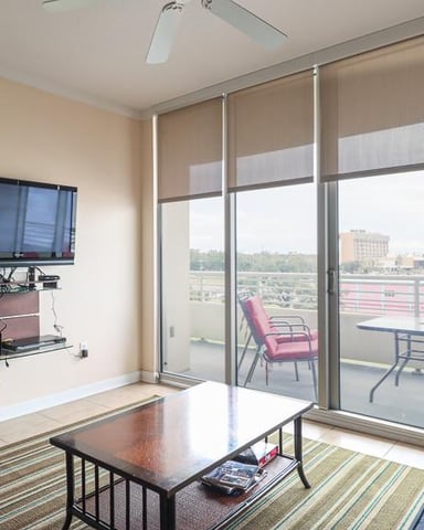 Modern living room with wall-mounted TV, patterned armchair, and floor-to-ceiling windows overlooking balcony with city view