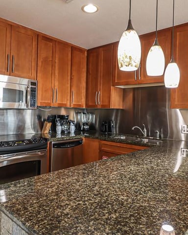 Modern kitchen with cherry wood cabinets, stainless steel appliances, granite countertop, and three pendant lights overhead.