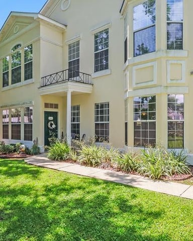 Cream-colored two-story house with black-trimmed windows, metal balconies, and manicured lawn with landscaping beds.
