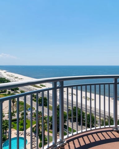 Curved balcony with metal railing overlooking sandy beach, ocean, and high-rise beachfront condominiums