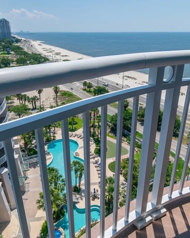 Oceanfront balcony view of beach, pool, and high-rise resort buildings with white railings