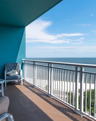 Oceanfront balcony with teal awning, seating, and metal railing overlooking beach and sea