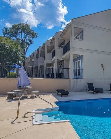 Modern beige apartment building with pool, lounge chairs, and umbrella on patio deck under blue sky