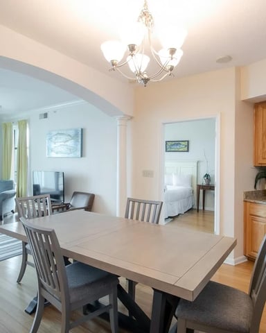 Open-plan living and dining area with kitchen, ocean-view balcony, and bedroom visible through archway