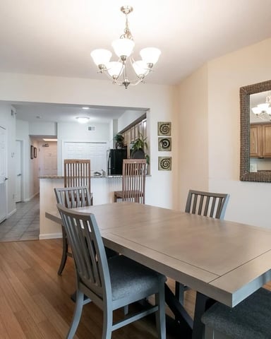 Dining room with light wood table, gray upholstered chairs, and open-plan view to kitchen and living areas