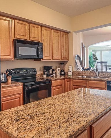 Kitchen with wood cabinets, granite countertops, black appliances, island, and open view to living area with patio doors
