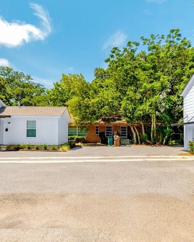 Courtyard with white modern houses, gravel driveway, mature trees, and clear blue sky