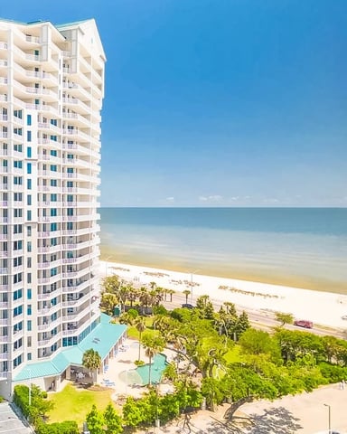White beachfront condominium tower with turquoise accents, pool, and sandy beach with ocean view