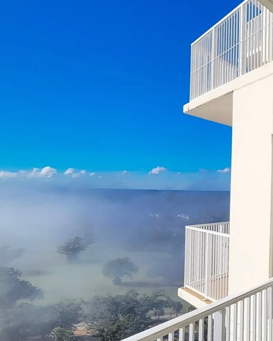 Modern white building with balconies overlooking misty valley landscape under clear blue sky