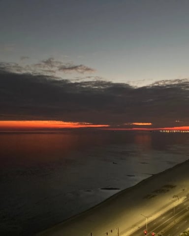 Sunset over ocean with illuminated beach and coastal promenade below