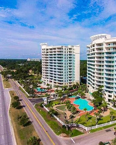 Beachfront resort with two high-rise towers, pool, and wide sandy beach along coastal highway