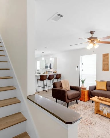 Open-plan living room with brown sofa, armchair, wooden coffee table, and staircase with wood treads leading upward.
