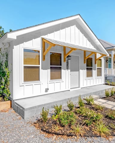 Modern white cottage with yellow pergola, front porch, and landscaped gravel yard under clear blue sky