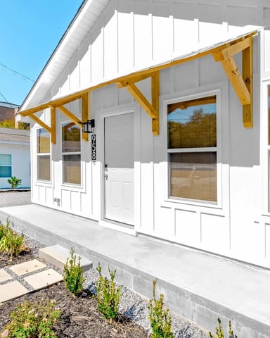 Modern white house exterior with yellow wooden pergola, concrete patio, and landscaped front yard with stepping stones