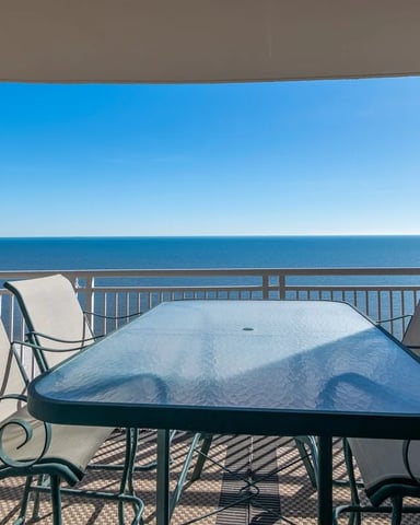 Oceanfront balcony with metal chairs, glass table, and clear sea view under blue sky